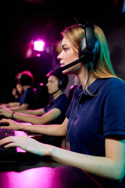 在电子体育俱乐部玩网络游戏时 以使用键盘的免提耳机为核心的年轻女性电脑游戏玩家 — 图库照片