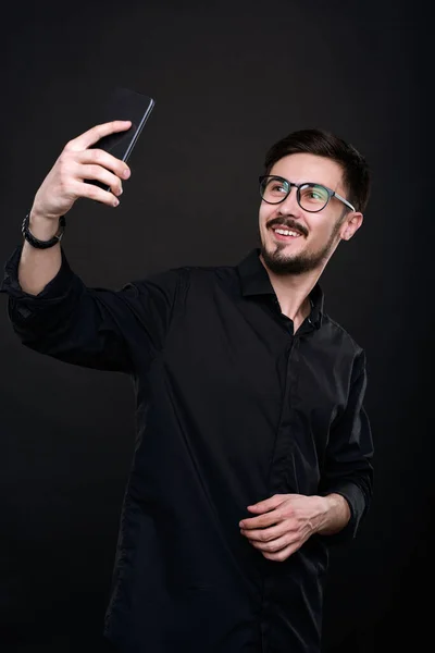 Jovem Bonito Positivo Óculos Tirando Selfie Camisa Preta Smartphone Contra — Fotografia de Stock