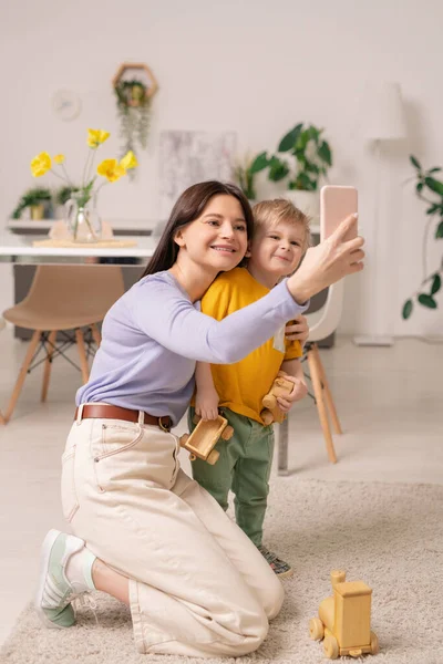 快乐的年轻女子和她可爱的小儿子一边看着智能手机摄像头 一边在家里自我封闭 — 图库照片
