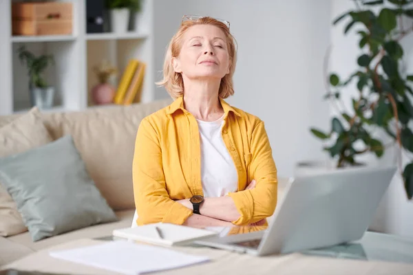 安详而成熟的金发女人穿着便服 在笔记本电脑前舒服地躺在沙发上 在家里做远程工作时闭上眼睛 — 图库照片