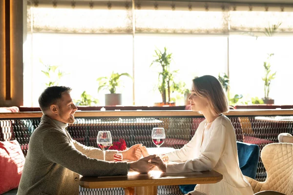 かなり若いです女性と彼女のボーイフレンド座っていますによってテーブルの前でお互いにと開催によって手 ロマンチックなデート — ストック写真