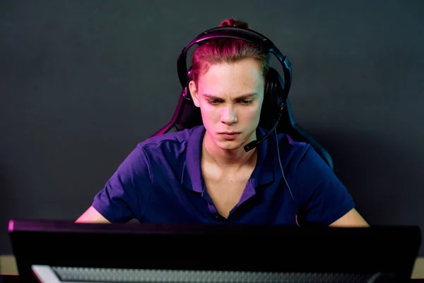 一个拿着话筒坐在电脑前玩网络游戏的严肃年轻人 — 图库照片