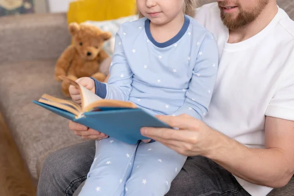 若いお父さんの家族と彼の可愛いです小さな娘で青いパジャマ読書面白い本を家でリラックスしながら寝る前に — ストック写真