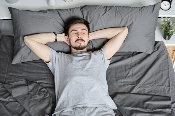 一个人睡在床上 一个留着胡子的年轻人双手反着头躺在床上 — 图库照片