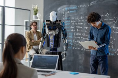 Sınıfın önünde dizüstü bilgisayarı olan zeki genç adam robot yeteneklerini ve özelliklerini sunuyor.