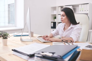 Ciddi genç bayan ofis yöneticisi bilgisayar ekranına bakarken masadan masaya yığınla kağıtla birlikte girdi