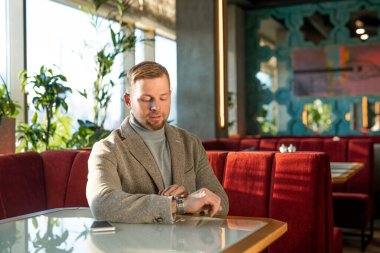 Kol saatine bakan zarif genç adam şık bir restoranda yumuşak kadife koltukta oturmuş randevusunu bekliyor.