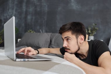 Karantina sitelerinde sörf yaparken dizüstü bilgisayara bakan sıkıcı genç adam.