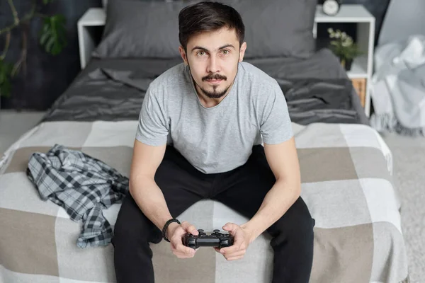 Joven Curioso Sentado Cama Usando Joystick Mientras Juega Videojuego Casa —  Fotos de Stock