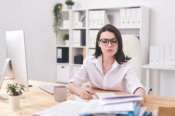 Young Serious Businesswoman Looking Financial Paper While Making Notes Notebook — Stock Photo, Image