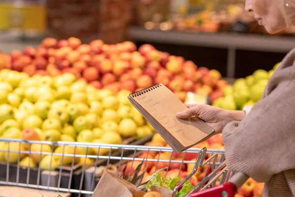 Зрелая Женщина Потребитель Блокнотом Над Пищевыми Продуктами Корзине Глядя Через — стоковое фото