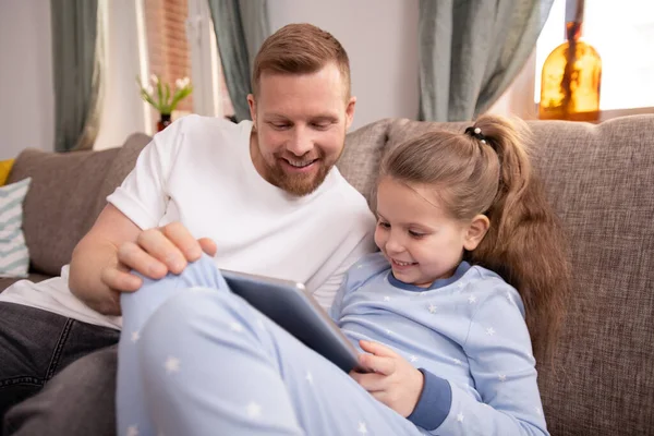 可爱的小女孩 带着触摸板 她的父亲一边看网上电影或卡通片 一边呆在家里检疫 — 图库照片