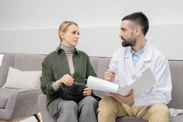 Joven Médico Confiado Whitecoat Haciendo Notas Documento Mientras Consulta Uno — Foto de Stock