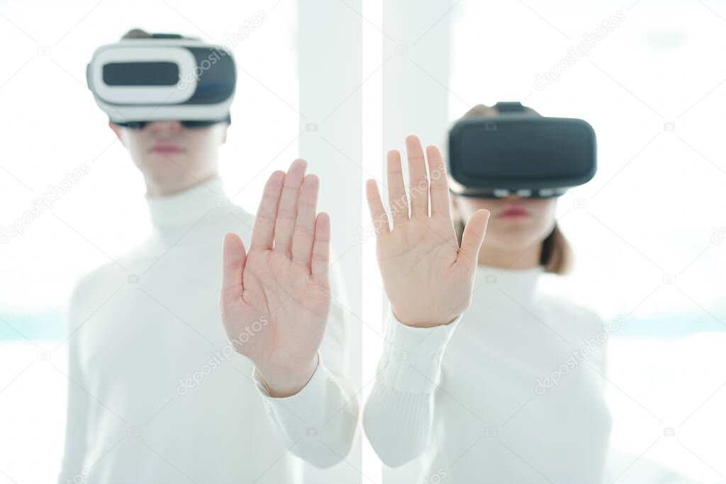 Palms of young male and female software developers in vr headsets keeping hands in front of camera while working in augmented realty