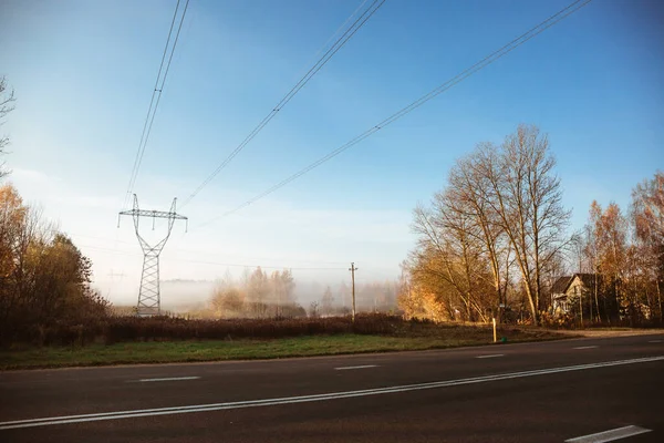 Линии электропередачи с электричеством на поле осенним утренним туманом — стоковое фото