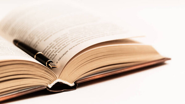 Черное и золотое дорогое перо лежит на открытой книге. Макро фото
.