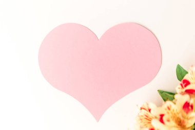 Beyaz arka planda sarı çiçeklerle süslenmiş büyük pembe bir kalp.