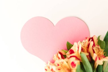 Beyaz arka planda sarı çiçeklerle süslenmiş büyük pembe bir kalp.