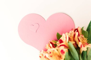 Beyaz arka planda sarı çiçeklerle süslenmiş büyük ve küçük pembe kalpler.