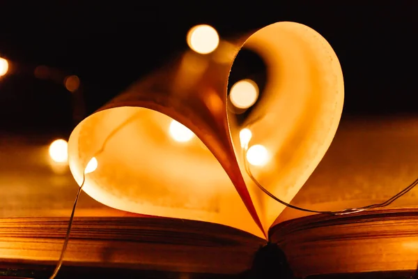 Powieść książki sztuki z prześcieradłami w kształcie serca ozdobione jasnymi światłami girlandy tła, symbol miłości — Zdjęcie stockowe