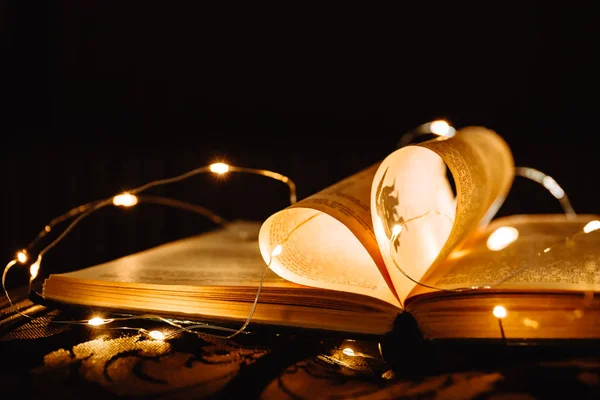 Powieść książki sztuki z prześcieradłami w kształcie serca ozdobione jasnymi światłami girlandy tła, symbol miłości — Zdjęcie stockowe