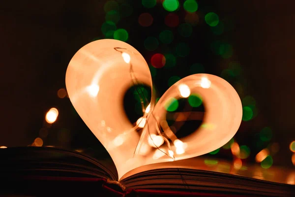 art book novel with sheets in the shape of a heart decorated with bright garland lights background, symbol of love
