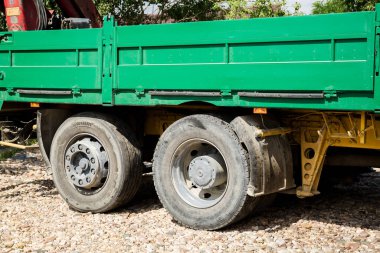 Üzerinde yeşil römork olan bir kamyonun iki büyük tekerleği yaz günü yakın plan çekilmiş.