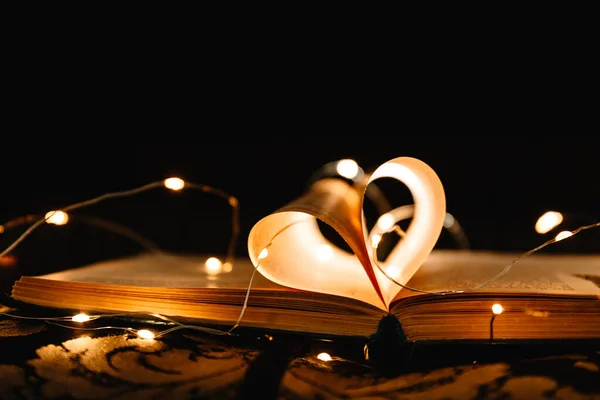 art book novel with sheets in the shape of a heart decorated with bright garland lights and highlights in the background, a romantic symbol of love, macro-shot
