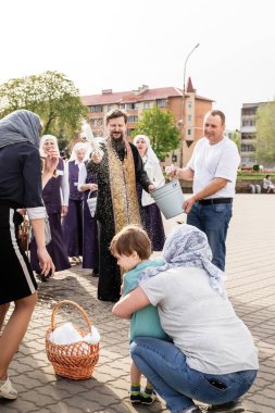 Beryoza, Belarus - 27 Nisan 2019: Rahip, Hristiyan dini geleneklerine göre, inançlıları ve Paskalya pastalarını, yumurta ve mumları kilisenin yakınında kutsal suyla boyadı..