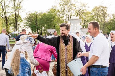 Beryoza, Belarus - 27 Nisan 2019: Rahip, Hristiyan dini geleneklerine göre, inançlıları ve Paskalya pastalarını, yumurta ve mumları kilisenin yakınında kutsal suyla boyadı..