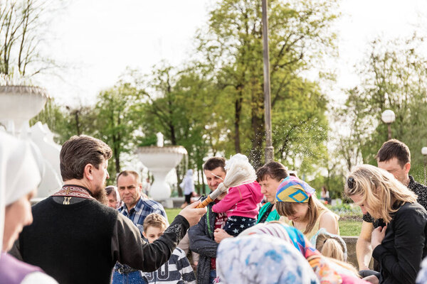 Берёза, Беларусь - 27 апреля 2019 года: Священник следует христианской религиозной традиции окропления верующих и их пасхальных тортов, разрисованных яиц и свечей, святой водой, возле храма
.