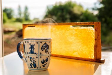 Bir fincan faydalı çay ve ballı sarı bal peteği. Soğuk algınlığı için şifalı bitkisel çay ve bal da dahil olmak üzere halk yöntemleriyle etkili bir tedavi. Yakın plan.