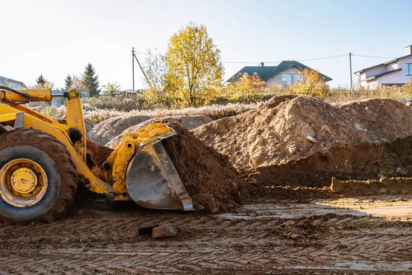 Büyük sarı tekerlek yükleyici yeni bir bina için bir parça arazi hizalıyor. Arazinin açık artırma için hazırlanması. Manzarayı düzleştirip inşaat için kum ekliyorum. Pankart Duvar Kağıdı.