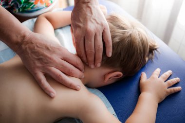 Doktor osteopat masaj terapisti küçük bir çocuğa masaj yapıyor. Eller arkaya ve rahim boynuna masaj yapsın. Yüzü olmayan yakın plan görüntü. Annesi bebeğine masaj yapıyor..