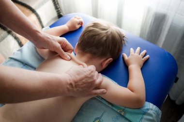 Doktor osteopat masaj terapisti küçük bir çocuğa masaj yapıyor. Eller arkaya ve rahim boynuna masaj yapsın. Yüzü olmayan yakın plan görüntü. Annesi bebeğine masaj yapıyor..