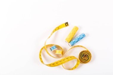 Bir santimetre bant ve iki makara sarı ve mavi iplik beyaz arkaplan üzerinde minimalist bir tarzda metin için bir yer. Dikiş, nakış, dikiş ve elbise kesmek için malzemeler. Stüdyo çekimi, yan görünüm.