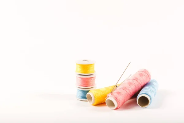 Three spools and bobbins of thread of yellow, blue and pink color with needles on a white background in a minimalistic style with a place for text. Items for needlework, embroidery and sewing. Studio shot, side view.