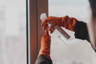Pencereyi temizleyen eldivenli ellerin yakın çekimi, virüse karşı antiseptik ve dezenfektanla tedavi edilmesi.