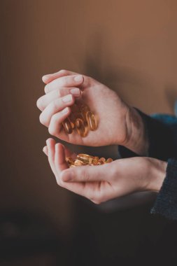 Büyük sarı vitamin kapsüllerini tutan ellerin yakın çekimi. Omega-3 vitaminleri. Balık yağının vücut için faydaları..