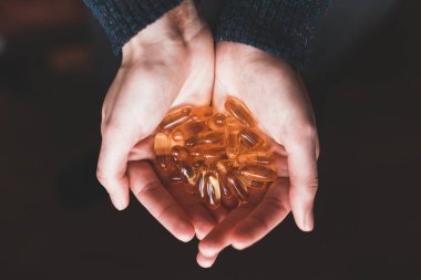 Büyük sarı vitamin kapsüllerini tutan ellerin yakın çekimi. Omega-3 vitaminleri. Balık yağının vücut için faydaları..