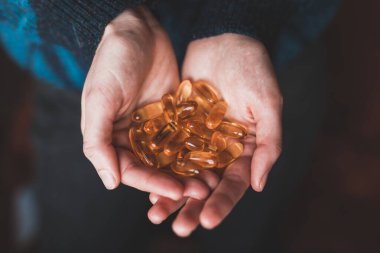 Büyük sarı vitamin kapsüllerini tutan ellerin yakın çekimi. Omega-3 vitaminleri. Balık yağının vücut için faydaları..
