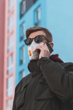 Virüs salgını sırasında boş bir sokakta gözlüklü ve koruyucu maskeli bir adam telefonla konuşuyor. Koruyucu maskeli bir adam telefonda konuşuyor..