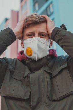 Virüs salgınının karantinası sırasında ıssız bir sokakta solunum cihazına koruyucu maske takmış dramatik bir yüz ifadesi olan bir adamın portresi..