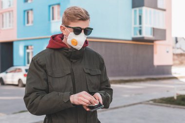 Koruyucu maskeli bir adam akıllı telefonunu ıslak bir antibakteriyel mendille temizliyor ve kendini virüsten koruyor. Koronavirüse karşı önleyici önlemler.