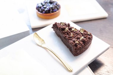 Çikolatalı pasta ve mermer tabakta yabanmersinli turta ve bir restoranda altın kaşık..