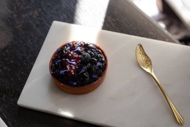 Mermerden yapılmış beyaz bir tabakta yaban mersinli turta ve altın kaşığın üzerinde fotokopi alanı ile parlayan güneş ışığı var..