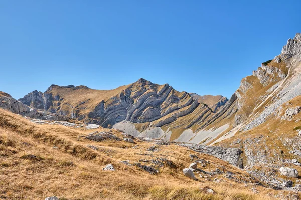 Rotsachtige bergen bedekt met herfstweide tegen de blauwe lucht — Stockfoto