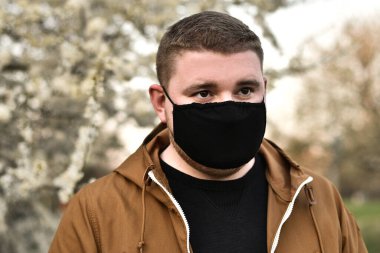 Çiçeklerin arka planında tıbbi maskeli ve eldivenli bir adam COVID-19