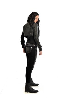 deri kıyafeti giymiş siyah saçlı kız tam uzunlukta portresi. Beyaz bir arka plan üzerinde ayakta poz.