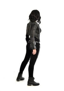 tam uzunlukta uzak kameradan bakan deri kıyafeti giymiş siyah saçlı kız portresi. Beyaz stüdyo arka plan üzerinde ayakta poz.